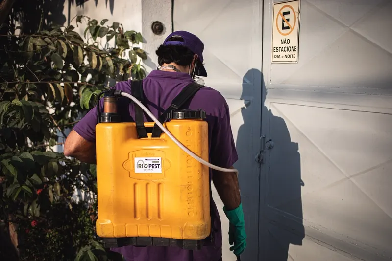 Técnico da Rio Pest Control com pulverizador costal chegando para atendimento em garagem